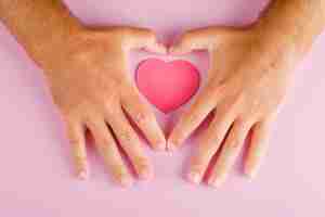 Free photo relationship concept on pink table flat lay. hands protecting paper cut heart.