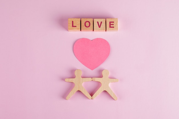 Relationship concept with paper cut heart, wooden cubes, human models on pink table flat lay.