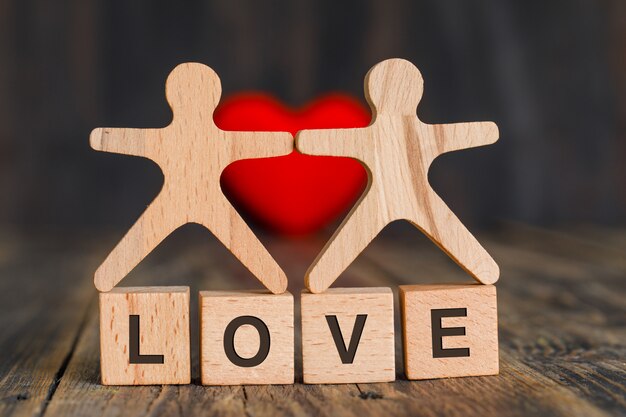 Relationship concept with red heart, wooden cubes and human models on wooden table side view.