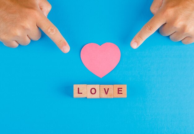 Relationship concept with wooden cubes on blue table flat lay. fingers showing paper cut heart.