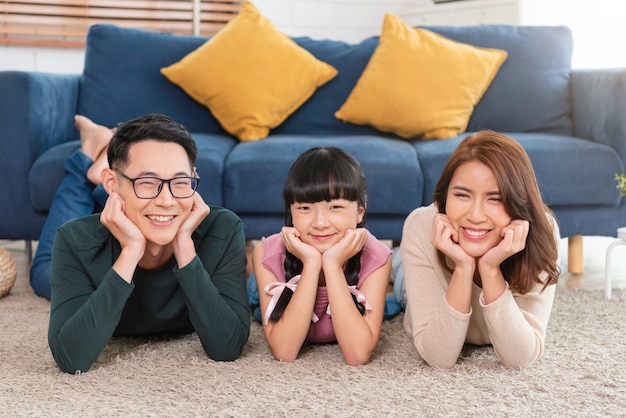 自宅のリビングルームのカーペットの上に幸せと笑顔で横たわっているアジアの家族をリラックスしてください。