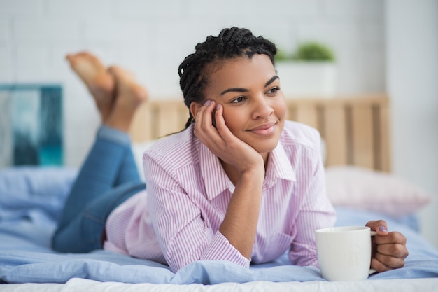 Relaxed African woman drinking tea in bed