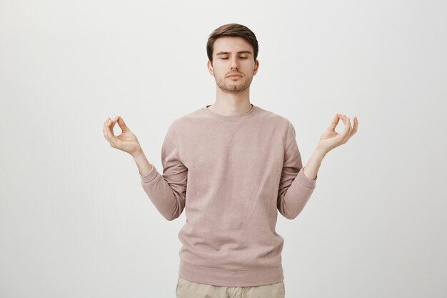 Relaxed attractive guy meditating, hold hands sideways with zen gesture