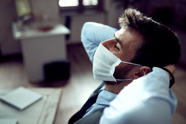 Relaxed businessman with protective face mask taking a break from work in the office