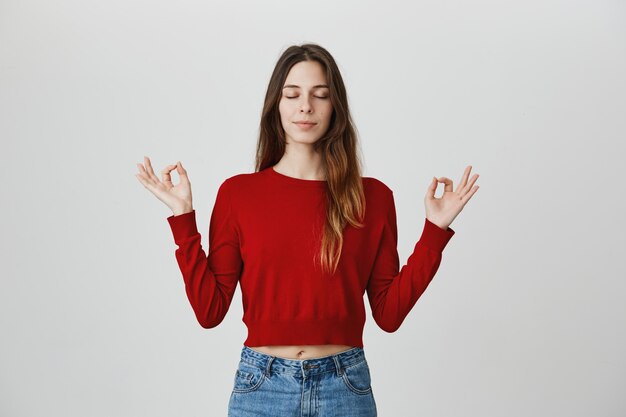 Relaxed and calm attractive woman meditating with hands spread sideways, closed eyes, do yoga