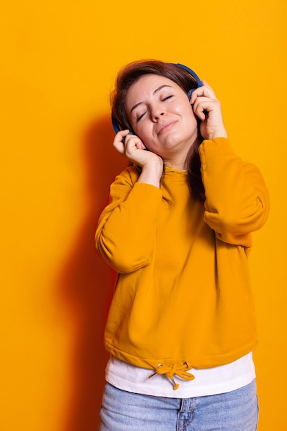 Relaxed cheerful woman enjoying song on headphones. positive adult listening to sounds and music, using headset to have fun at photoshoot in studio. young person relaxing with audio