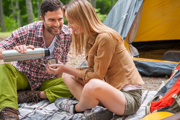 Relaxed couple enjoying in the forest and drinking coffee