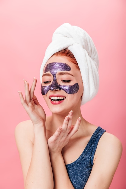 Relaxed european girl doing skincare treatment. Studio shot of positive woman with face mask isolated on pink background.