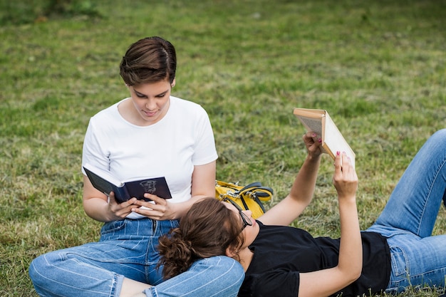 Free photo relaxed female friends reading on grass