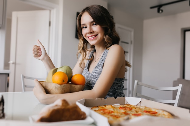 Relaxed girl embracing plate with fruits. glamorous curly woman posing with oranges and laughing.