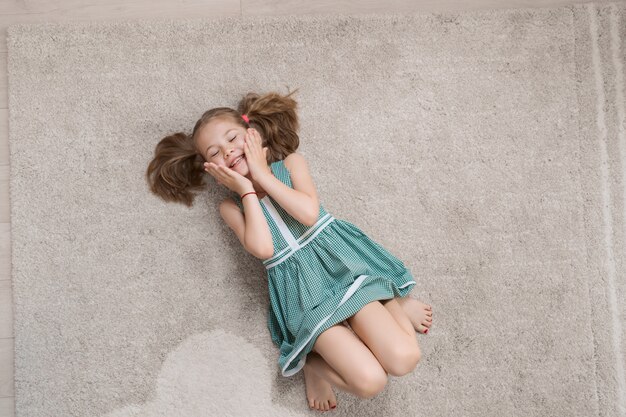 Расслабленная маленькая девочка лежит на полу в помещении и улыбается