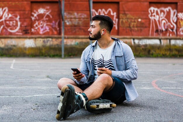 Relaxed male rollerskater with smartphone and disposal cup