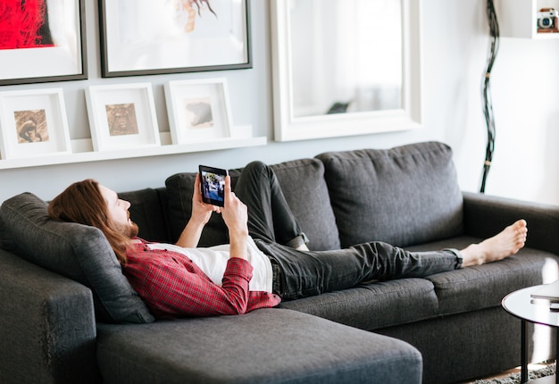 Relaxed man lying on sofa and watching video at home
