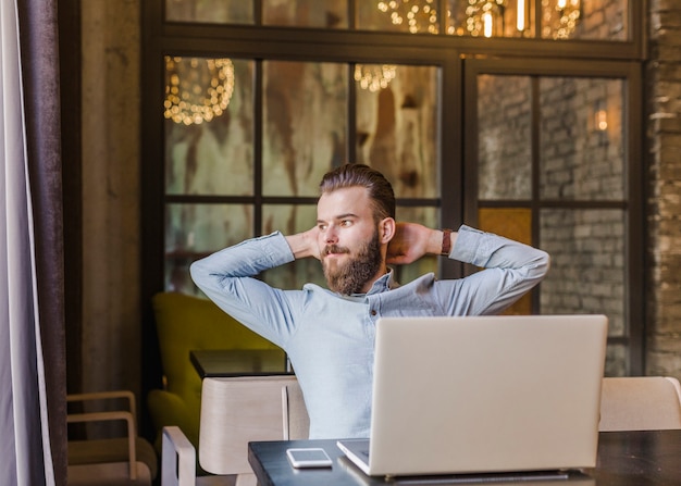 Relaxed man sitting in restaurant with laptop and cellphone on desk