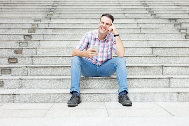 Free photo relaxed man using smartphone on city stairway