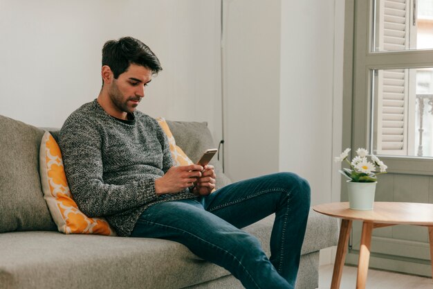 Relaxed man using smartphone on couch