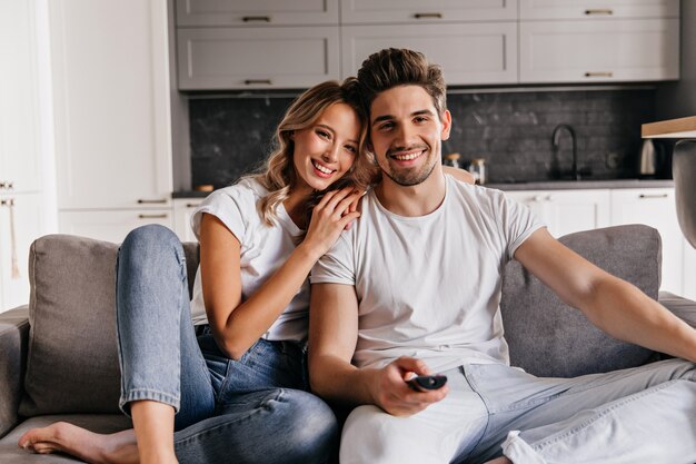 Relaxed man watch TV. Graceful blonde girl sitting on sofa with husband.