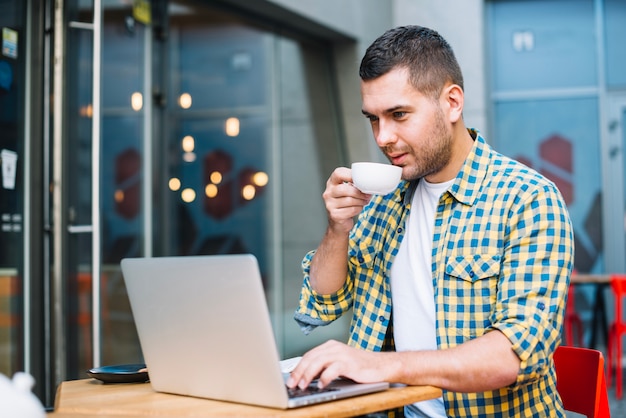 Relaxed man watching laptop while drinking coffee