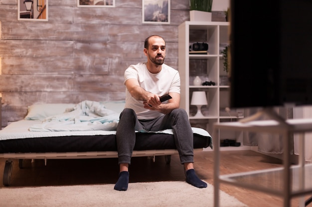 Free photo relaxed man watching tv at night from the edge of his comfortable bed.