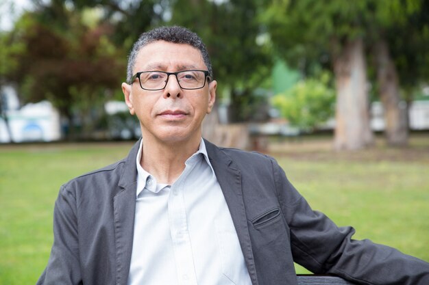 Relaxed middle-aged man posing at camera and sitting on bench