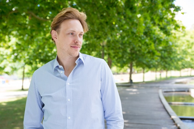 Relaxed peaceful guy in striped shirt walking through park