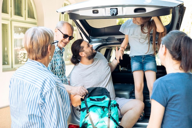 Persone rilassate che si preparano a partire all'avventura, mettendo borse da viaggio e valigie nel bagagliaio dell'auto. grande famiglia con genitori, nonni e bambino piccolo in viaggio per le vacanze estive.