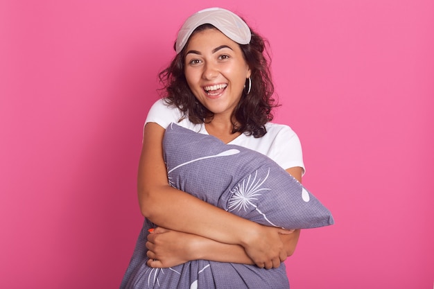 Relaxed sensual happy young woman hugging gray pillow, looking at camera with charming smile