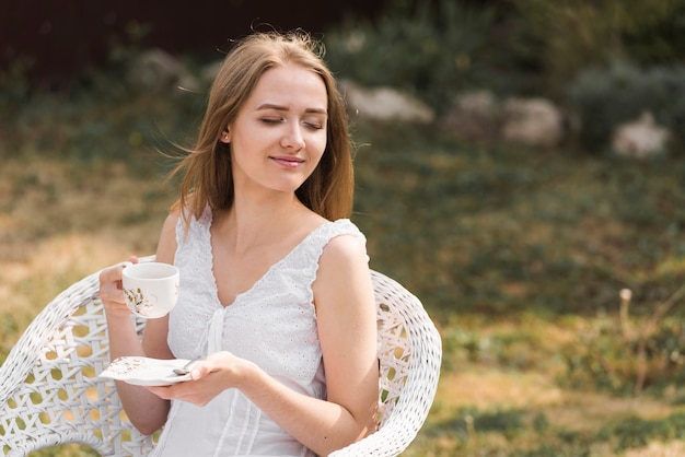 정원에서 커피를 즐기는 편안한 웃는 금발의 젊은 여자