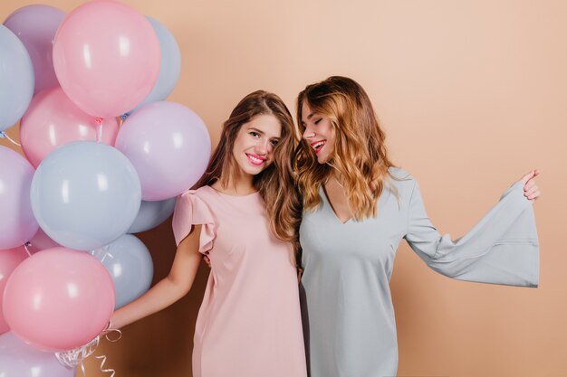 Relaxed woman in blue attire waving hands while posing at event with friend