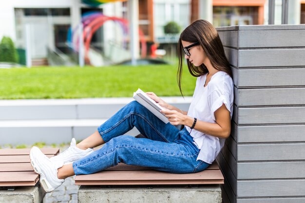 日没のベンチに座ってハードカバーの本を読んでリラックスした女性