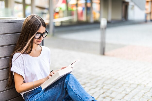 Relaxed woman reading a hard cover book at sunset sitting on a bench