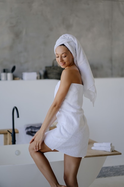 Relaxed young female model in white towel, feels refreshed after taking shower