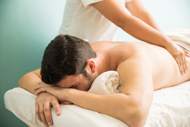 Расслабленный молодой человек получает массаж в оздоровительной и спа-клинике