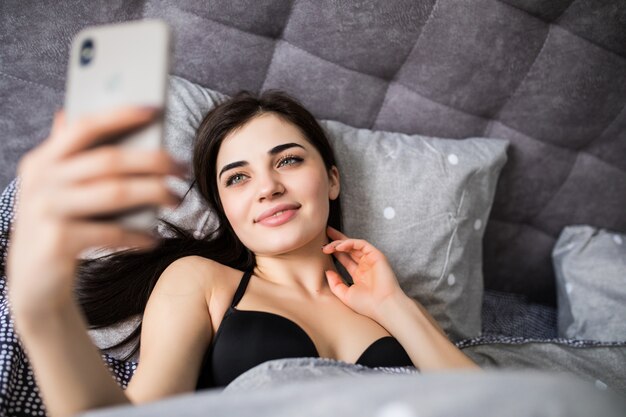 Relaxed young woman at home with phone on white bed