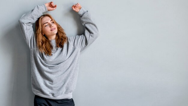 relaxed young woman leaning on grey wall with her raised hands