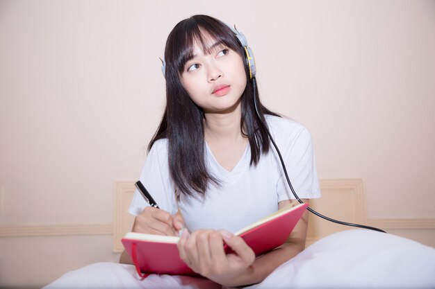 Relaxed young woman in pajamas writing diary on her bed 