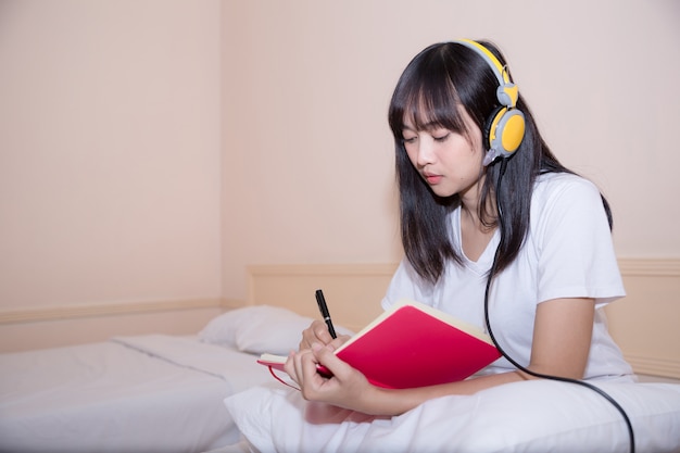 Relaxed young woman in pajamas writing diary on her bed 