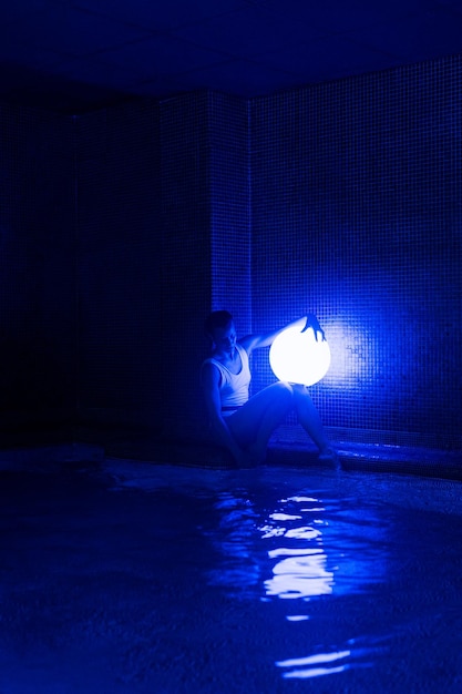 Расслабленная молодая женщина в бассейне с неоновым светом