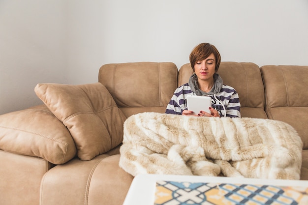 ソファの上で彼女のタブレットを使用して、リラックスした若い女性