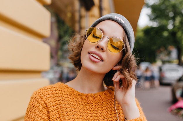 Relaxed young woman with pale skin enjoying music with eyes closed standing on the street background