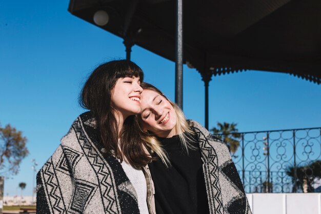 Relaxing cheerful girls cuddling in plaid