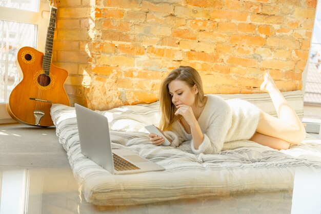 Relaxing at home. Beautiful young woman lying on mattress with warm sunlight. Caucasian blonde female model has weekend time for resting