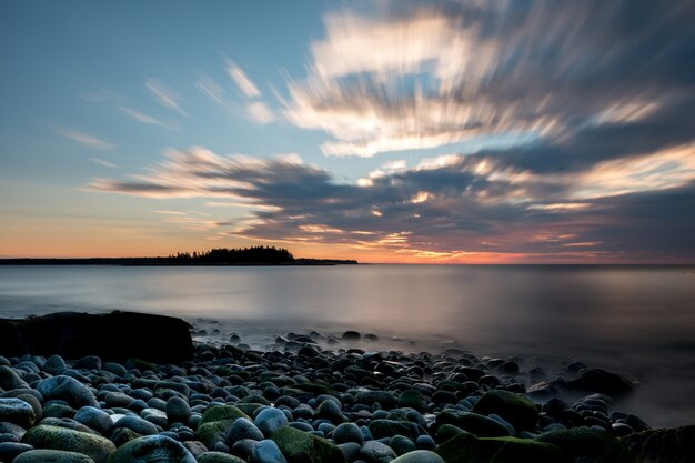 Relaxing scene of a seashore under the cloudy sky and the sun setting in the