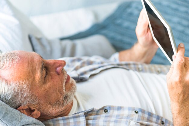 Расслабляющий старший человек, глядя на цифровой планшет
