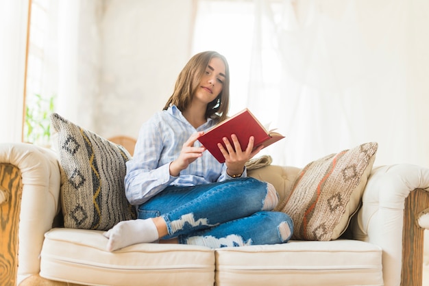 Relaxing woman sitting on sofa reading novel