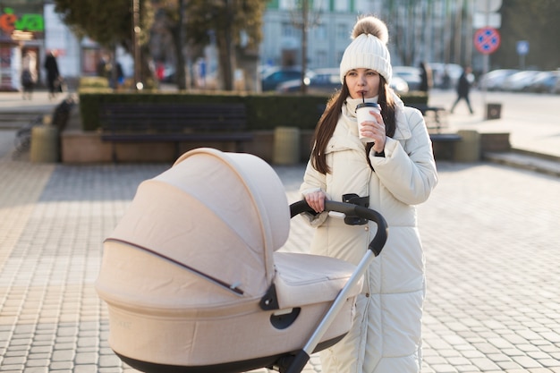 歩くことにコーヒーを持っているリラックスした若い母