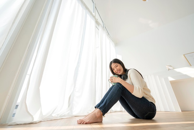 Relex and peaceful asian woman enjoy weekend with music headphone morning sunlight near window home background