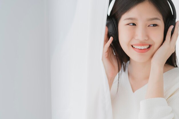 Relex and peaceful asian woman enjoy weekend with music headphone morning sunlight near window home background