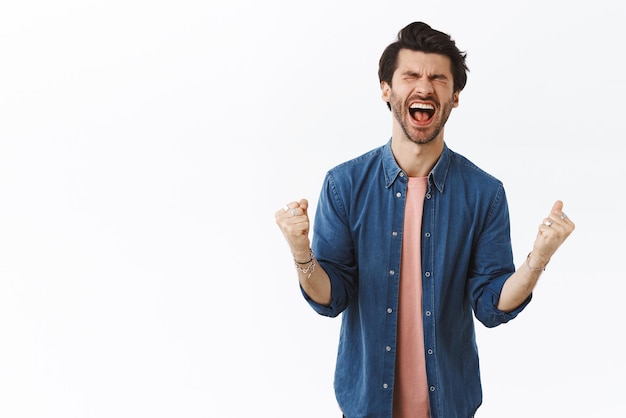 Free photo relieved happy lucky goodlooking man achieve prize winning dream came true close eyes and scream from happiness and joy clench hands as fist pump triumphing and celebrating amazing news