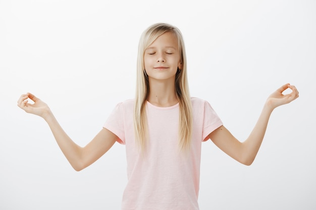 Free photo relieved smiling little woman meditating, child trying yoga